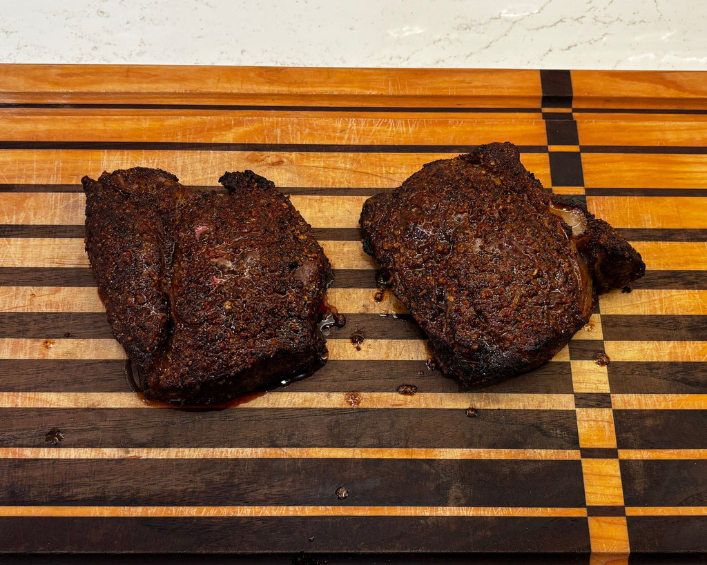 Two pieces of steak on a wooden cutting board with black and yellow stripes.