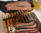 Person holding sliced brisket with a cutting board and tools in the background